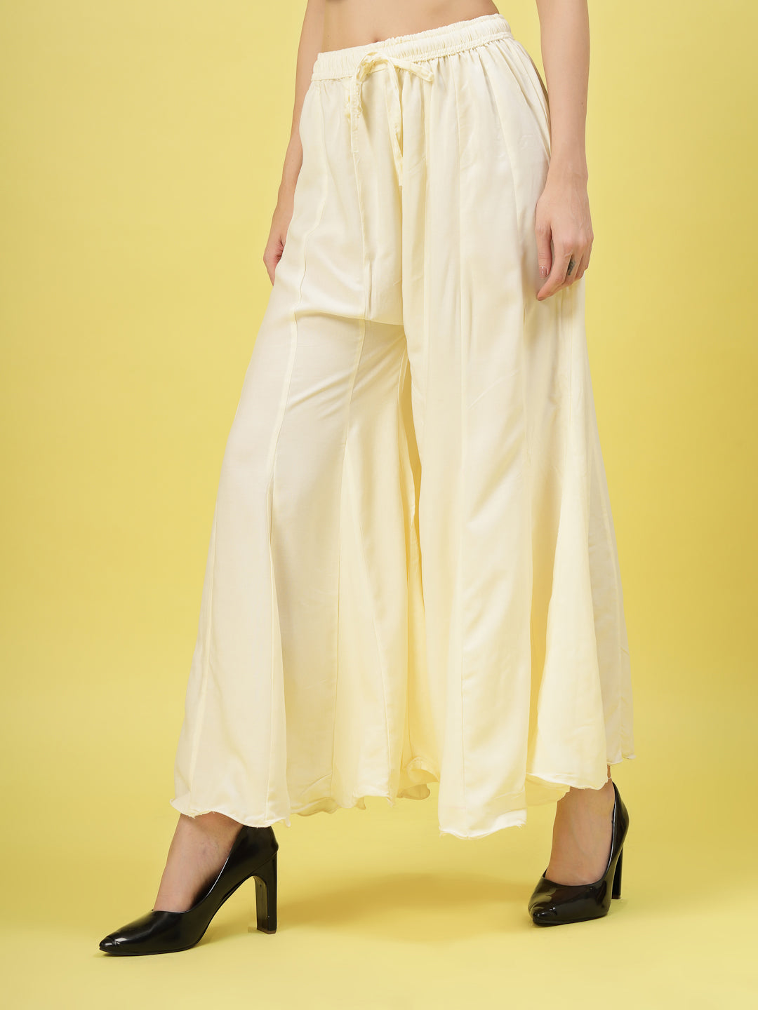 Women solid cream flared rayon sharara with elasticated waistband and drawstring closure.