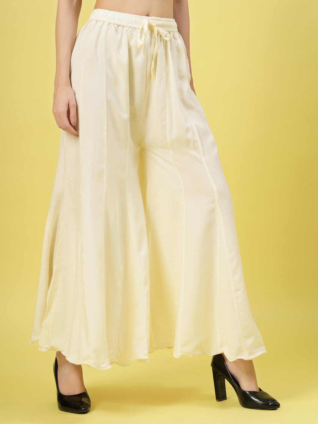 Women solid cream flared rayon sharara with elasticated waistband and drawstring closure.