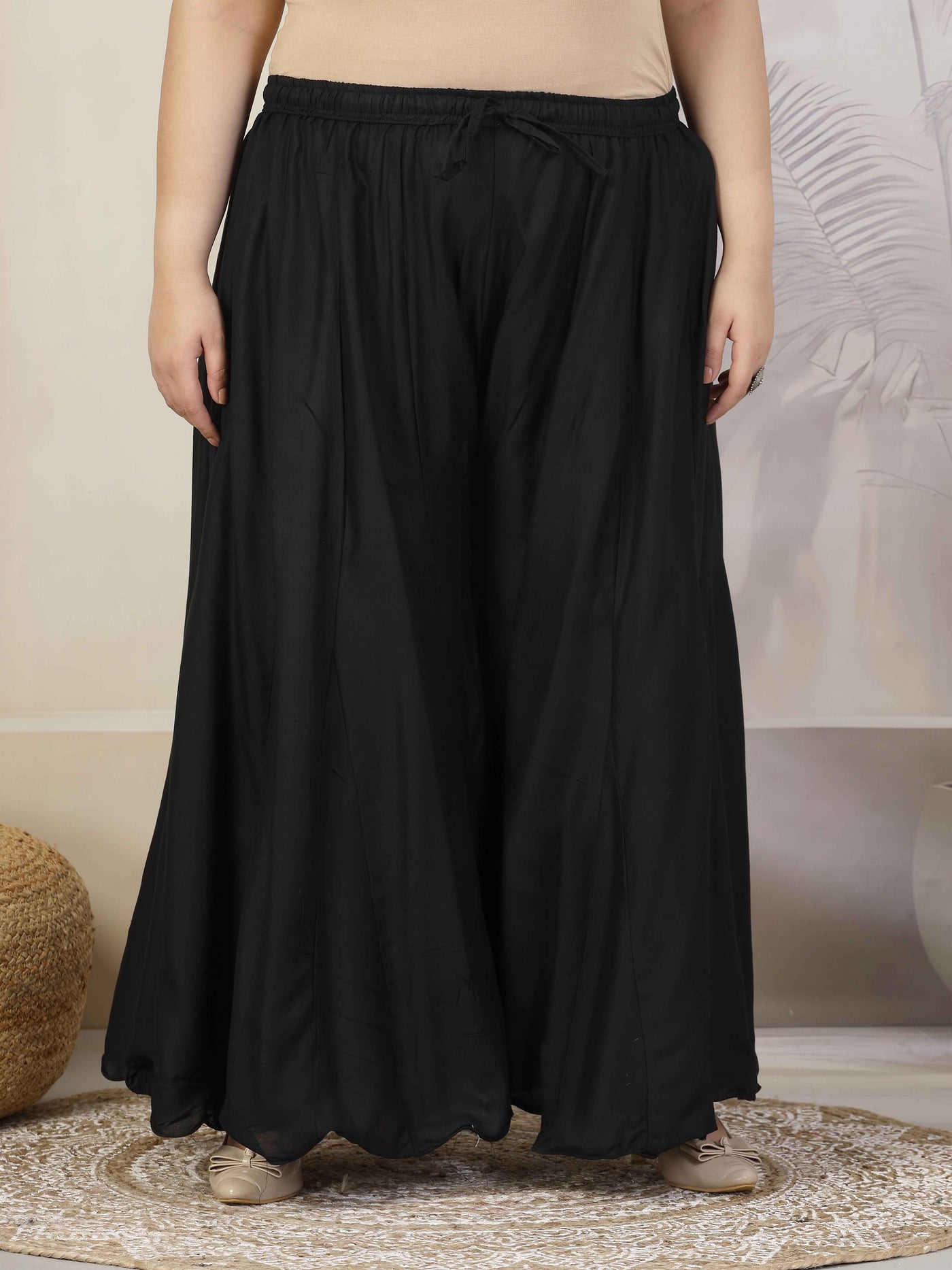 Women solid black flared rayon sharara with elasticated waistband and drawstring closure.