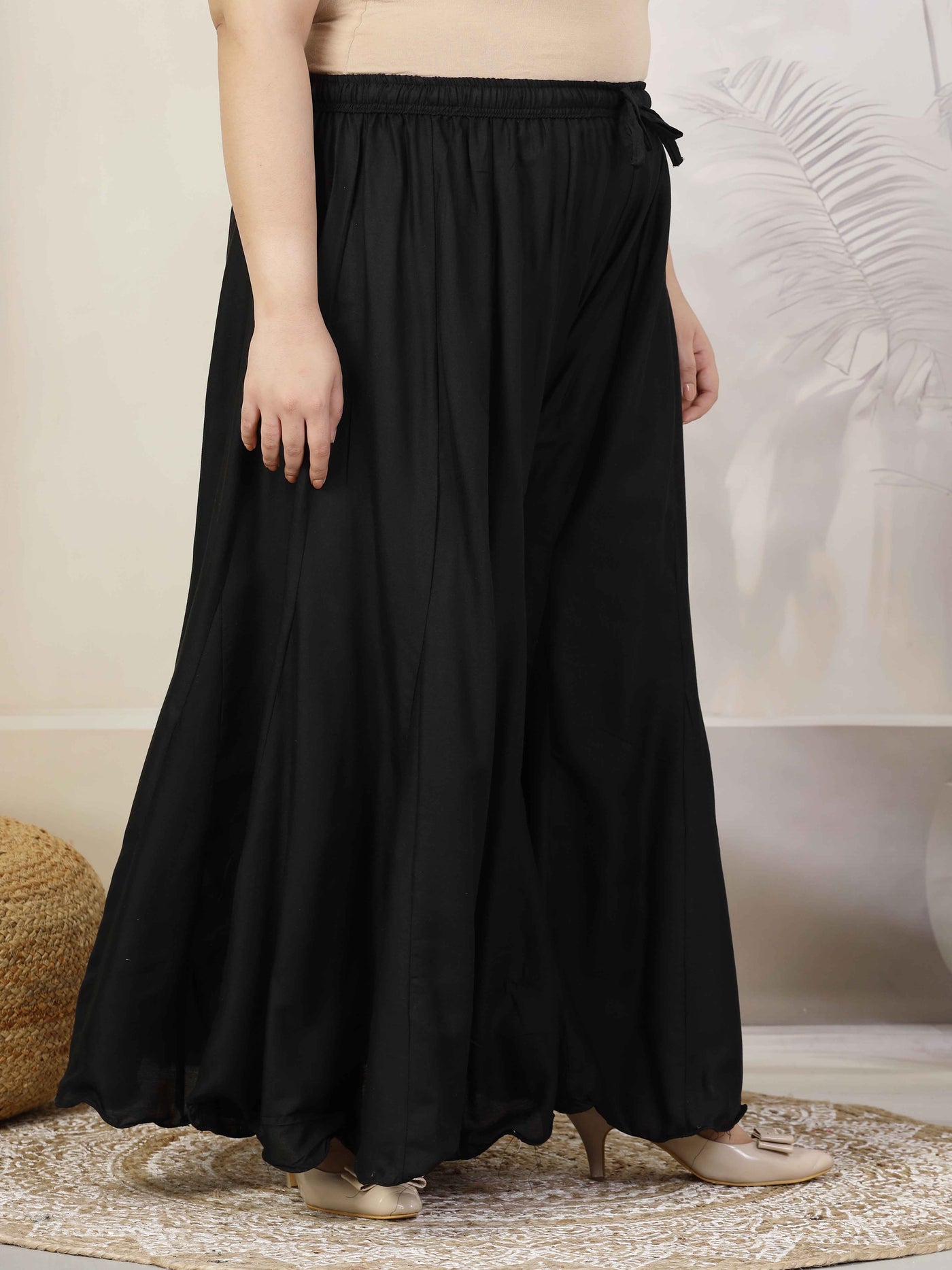 Women solid black flared rayon sharara with elasticated waistband and drawstring closure.