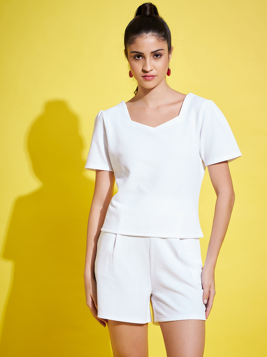 White self design top with V-neck and short sleeves paired with white mid-rise shorts featuring an elasticated waistband.